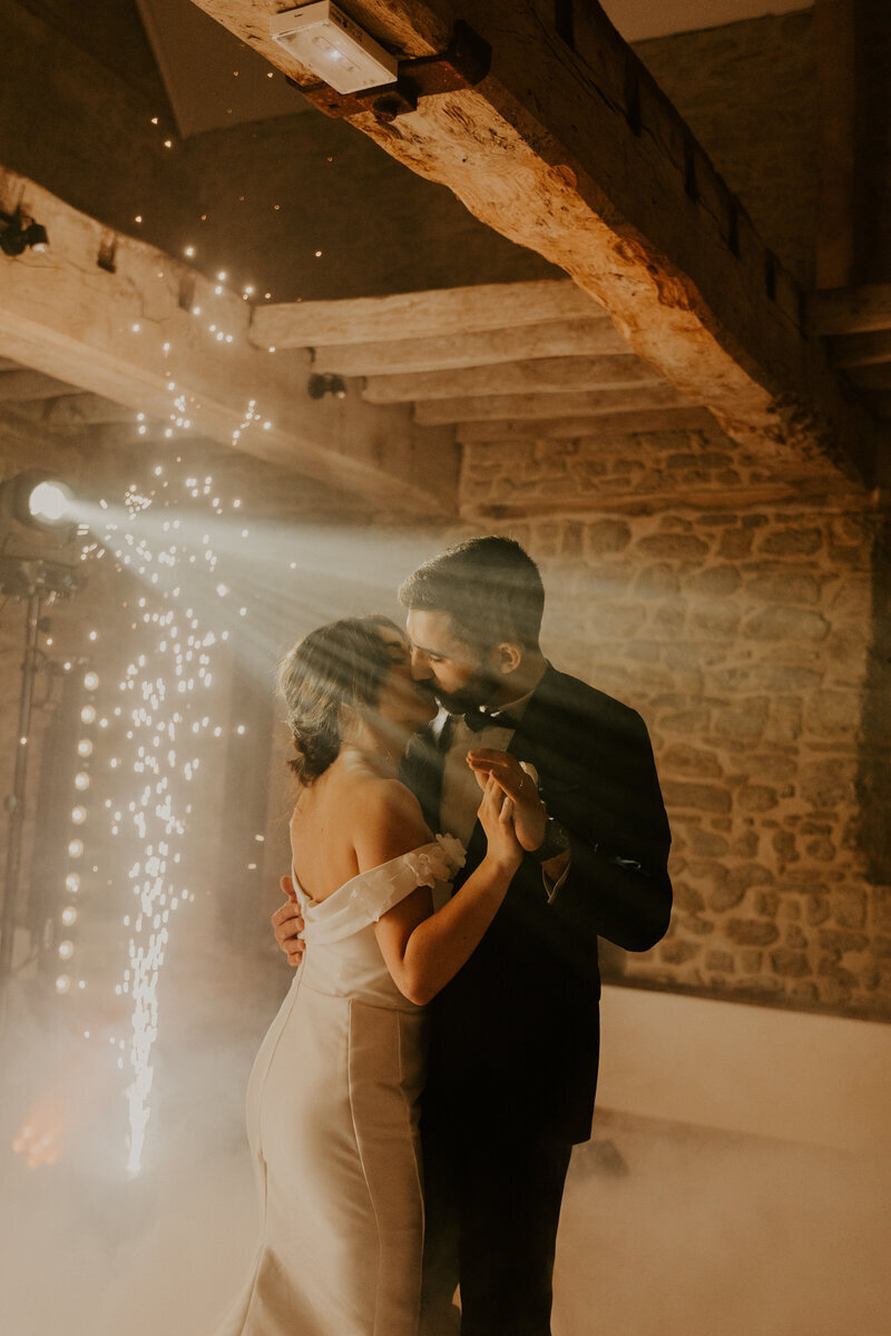 Mariés s'embrassant et dansant en même temps pour l'ouverture de bal, sous les projecteurs dans une ambiance tamisée. Photo issue du shooting photo mariage en Vendée.