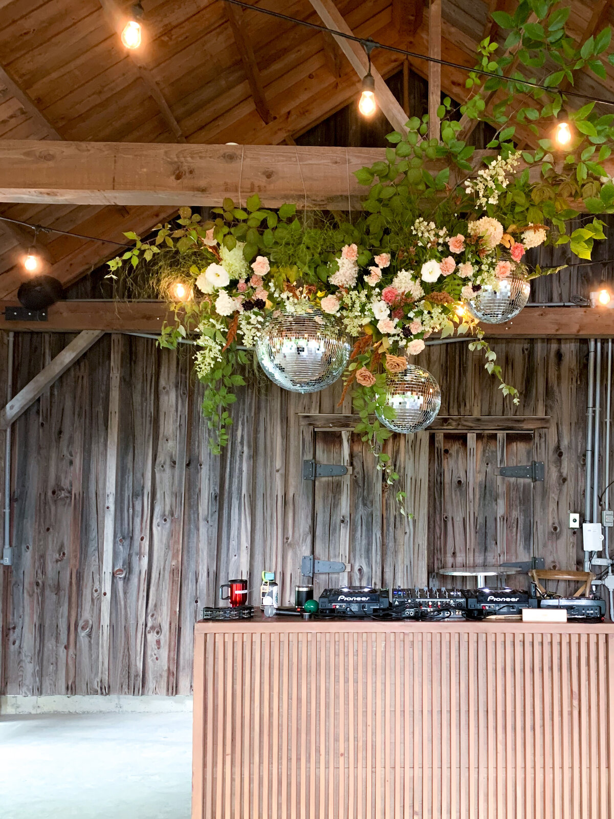 A lush flower arrangement is suspended with a disco ball at a barn wedding near Montreal. 
