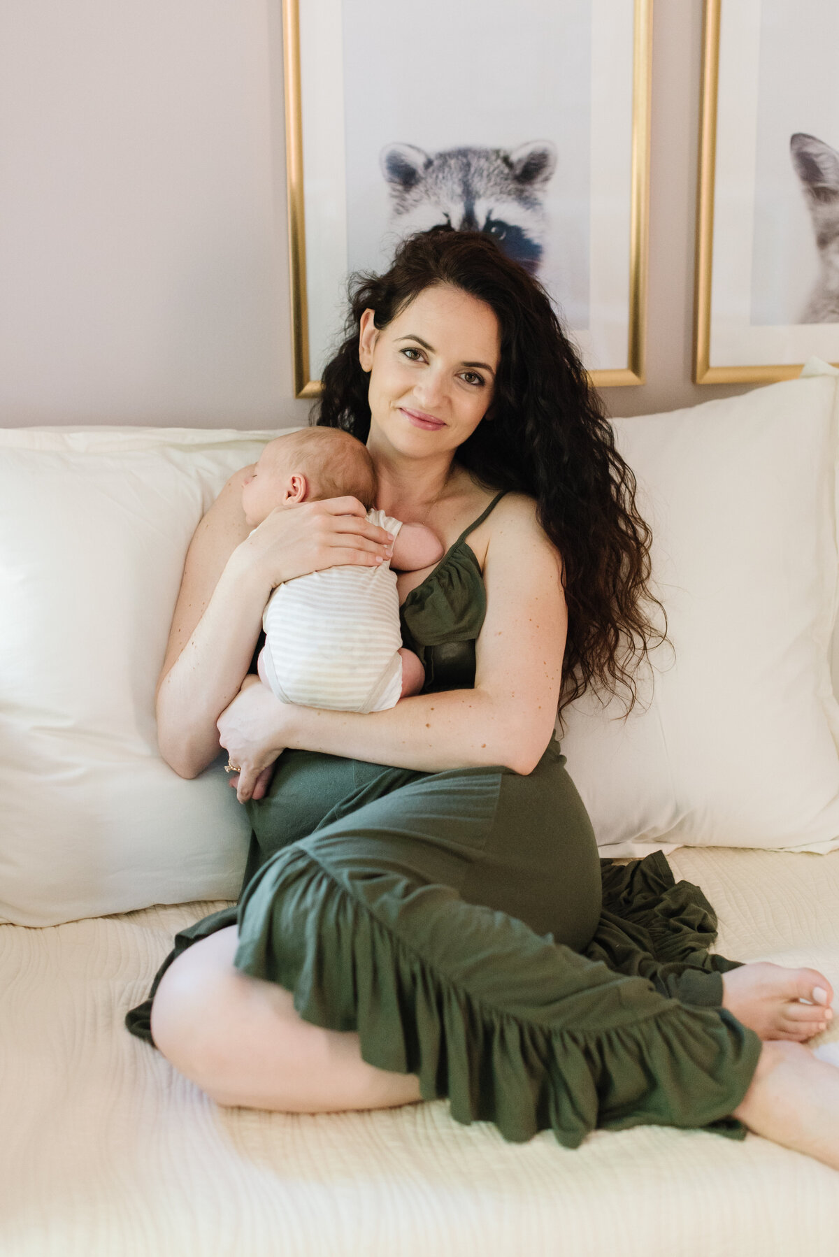 Mother in green dress holding baby on cream couch and smiling