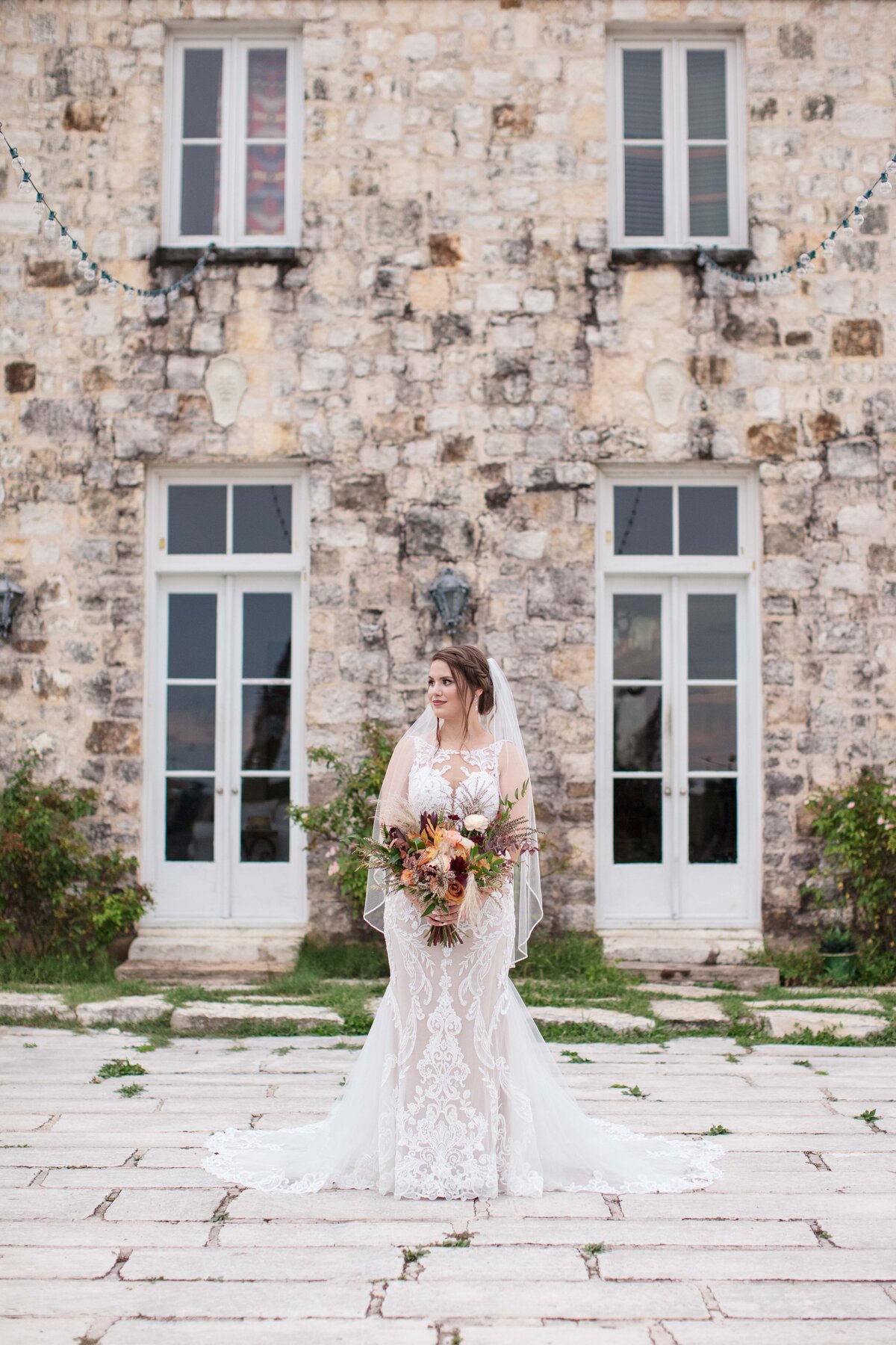 bride in San Marcos Texas stands  with flowers and large windows by Firefly Photography
