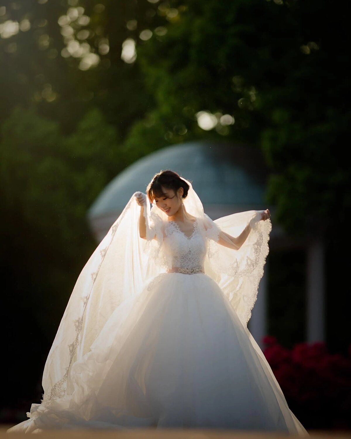 A bride in a stunning wedding gown adjusts her veil in the gentle light of sunset, with a serene expression on her face.