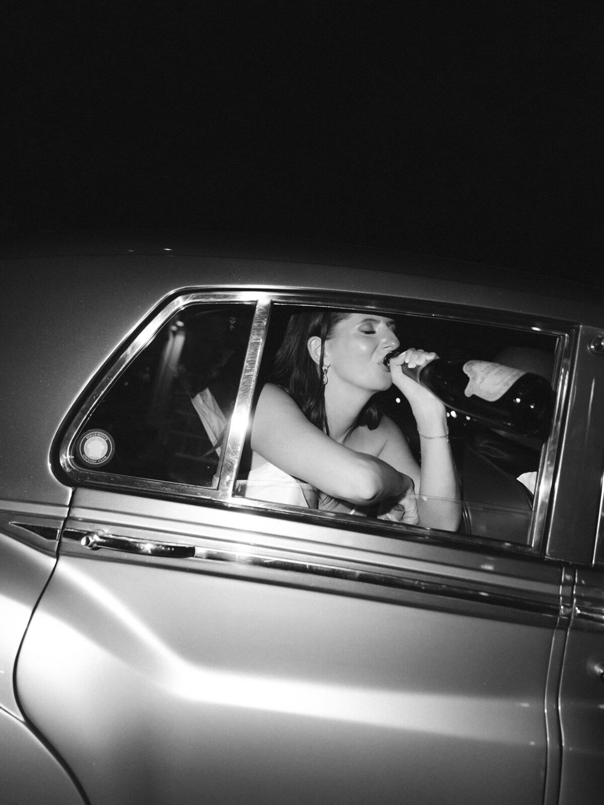 bride drinking from champagne bottle in the vintage exit car