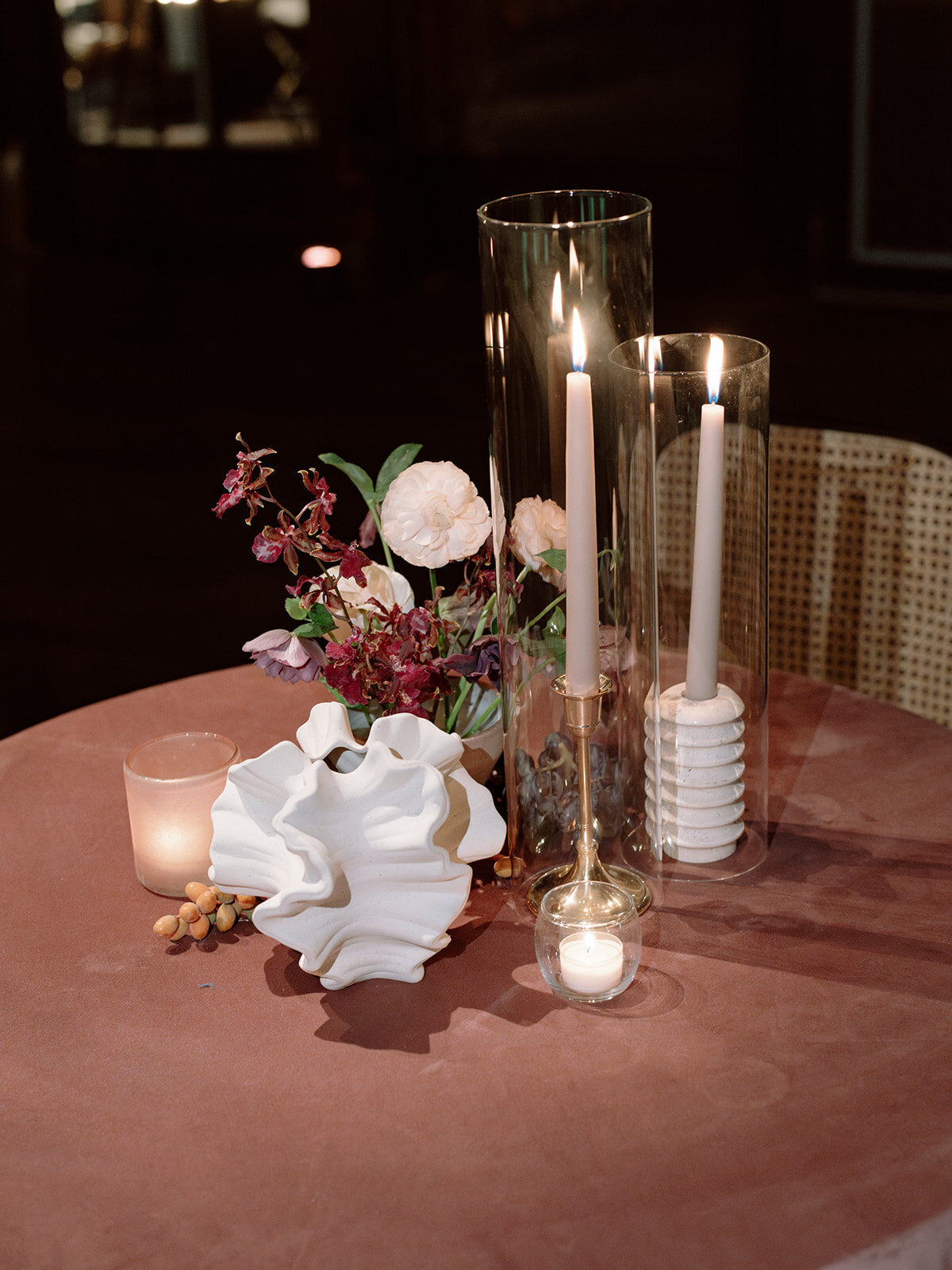 Clustered and styled floral arrangements, fruits, and art pieces for fall wedding reception. Low centerpieces mixed with ikebana arrangements and bud vases decorate the reception tables at this fall wedding. Floral centerpieces featuring orchids, ranunculus, sweet peas, and bittersweet. Styled wedding tables with fruits, curated candles, and floral arrangements. Tasteful fall color palette of copper, ruby, gold, burgundy, rust, and lavender. Design by Rosemary & Finch Floral Design in Nashville, TN.