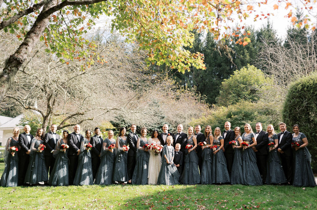 Large wedding party poses together under fall foliage with coordinated slate gowns and tuxedos, photographed in Highlands, NC.