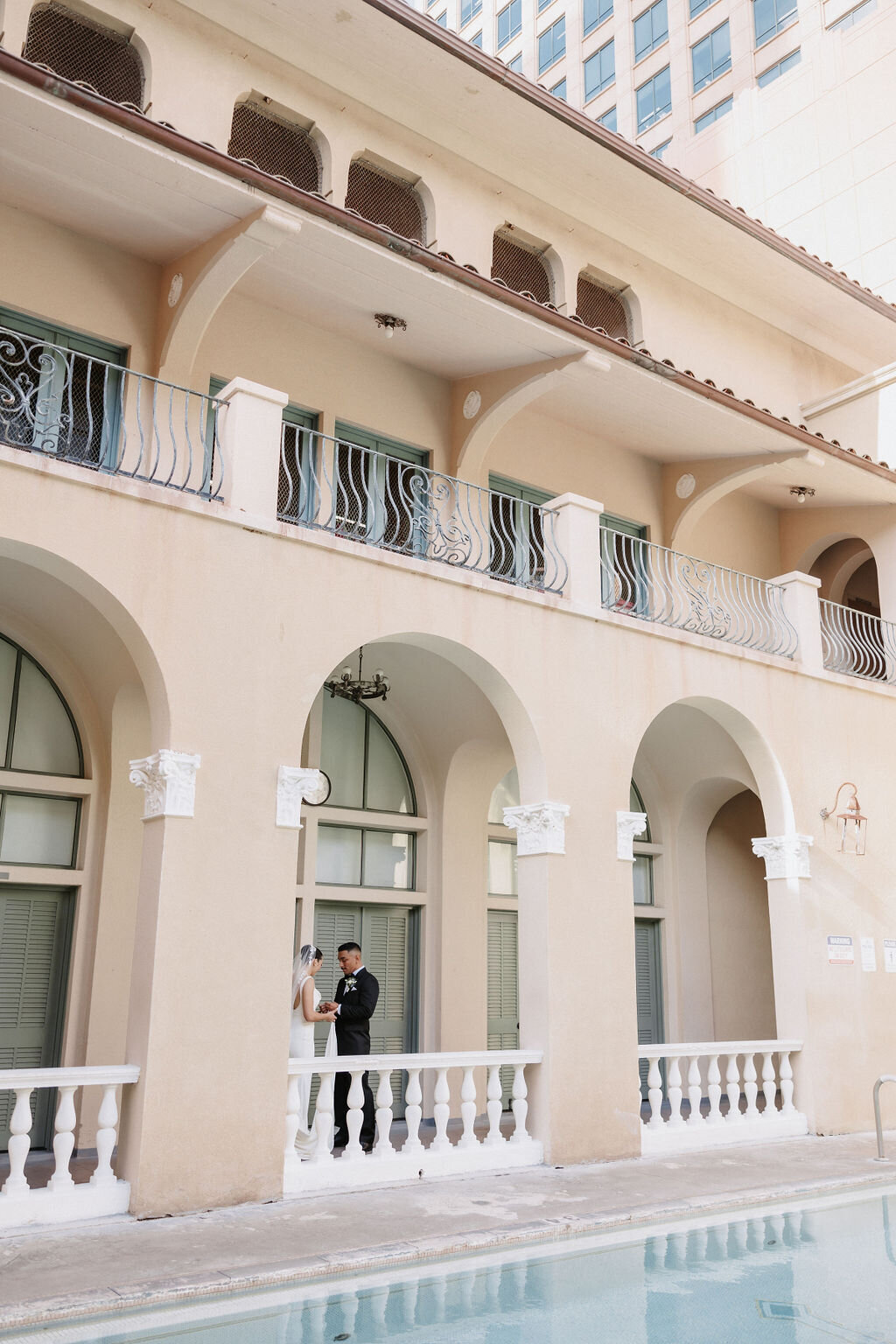 bride and groom facing each other under arches by the pool at cafe julia hawaii