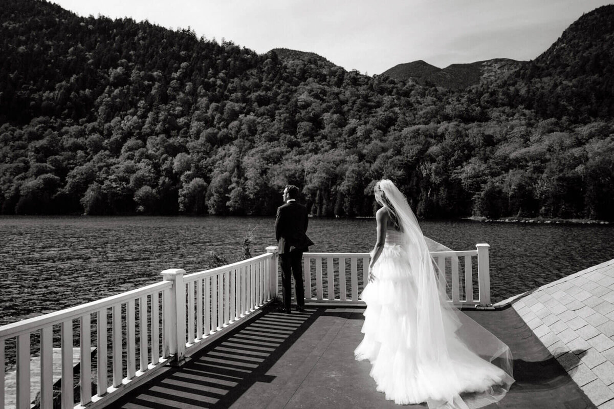 Black and white photo of the groom and the bride standing on a terrace, overlooking waters and mountains, at The Ausable Club.