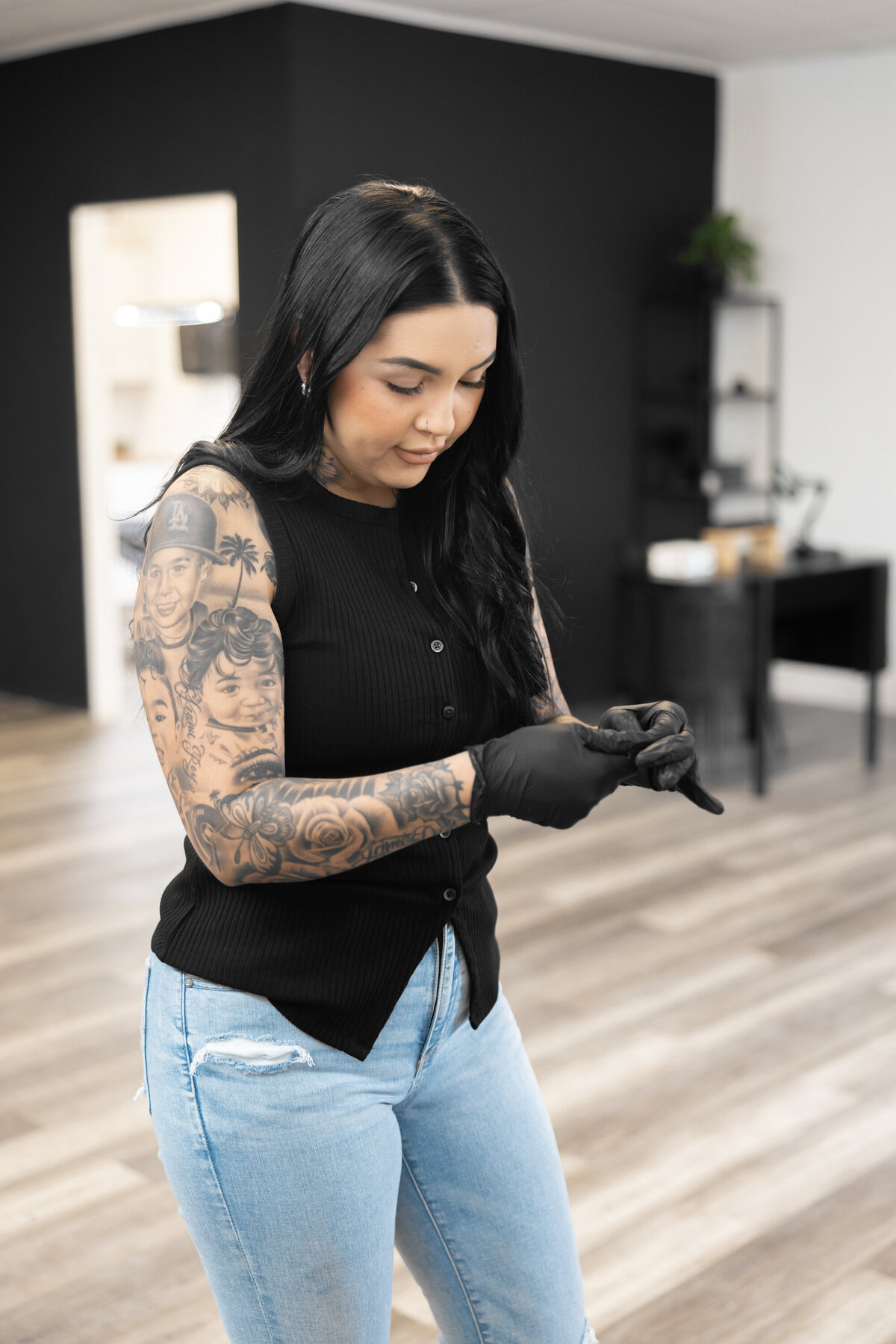 Woman with dark hair and tattoos smiling while standing in a salon workspace. Photograph by Yucaipa branding photographer Kaitlyn Dawn Photography.