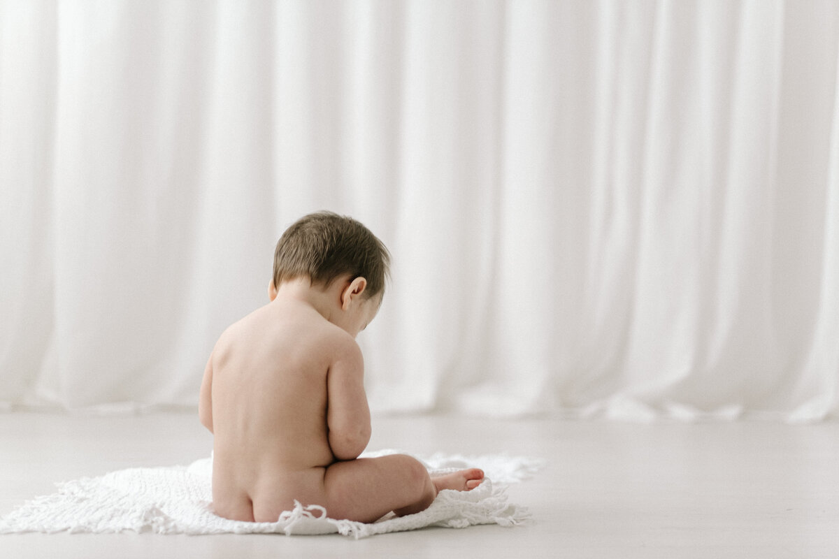 Naked baby sitting on the floor of a photo studio near Bristol