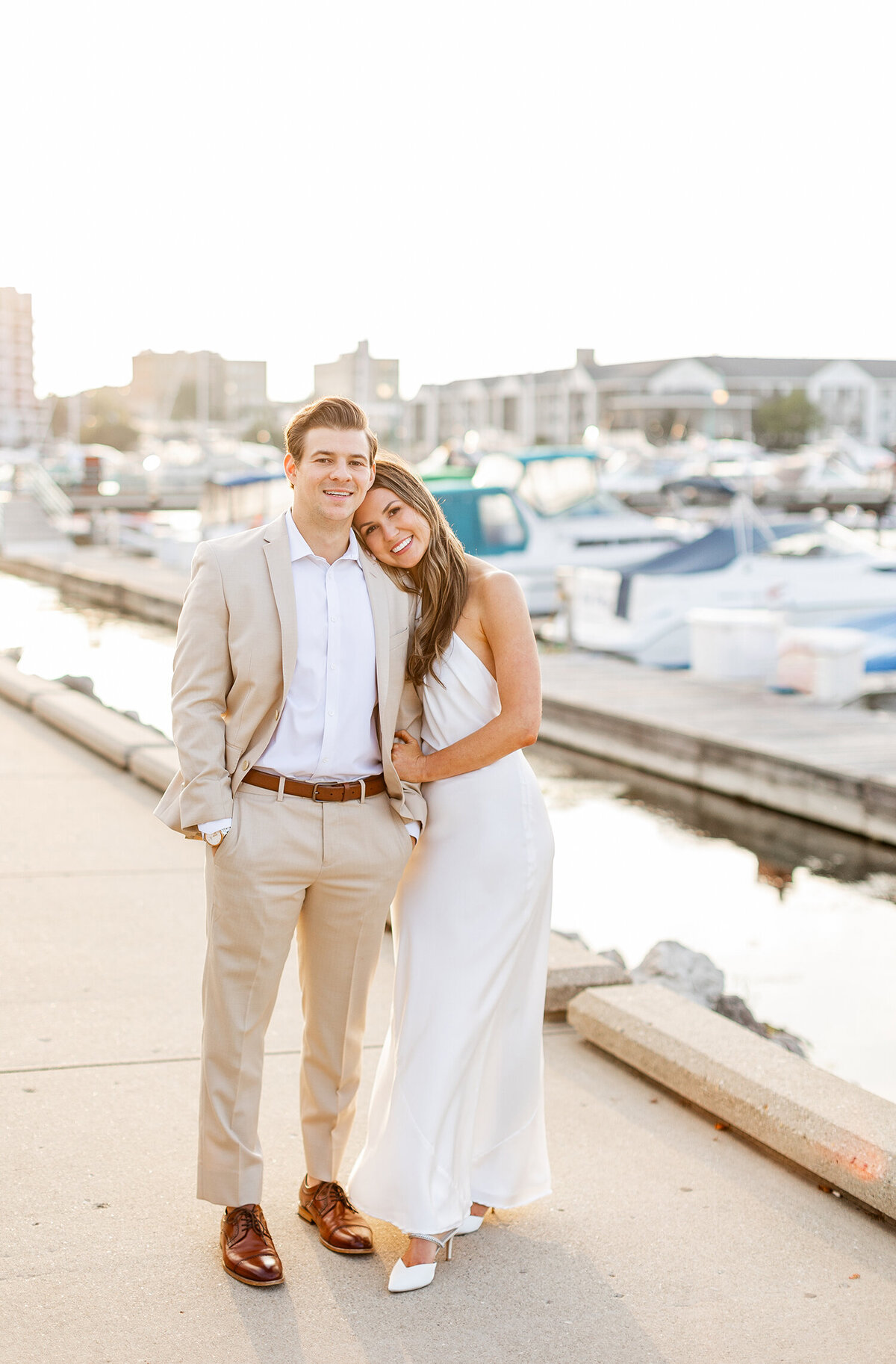 smiling couple stands on a marina dock at sunset