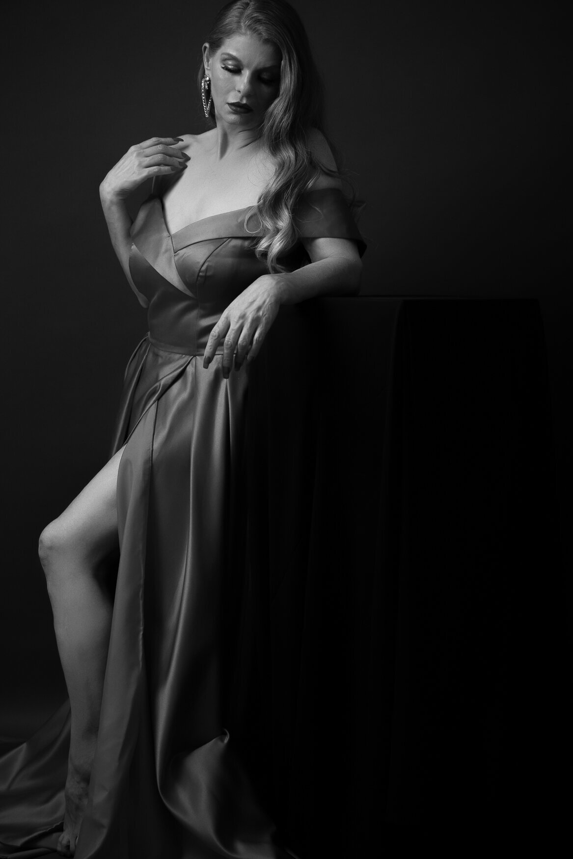 Woman with long curly hair posing looking down and with one arm touching her shoulder