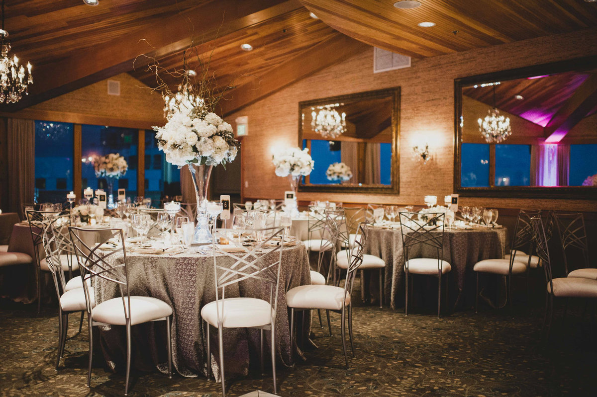 Romantic candle lit white winter wedding reception with silver Chameleon chairs and silver specialty table linens, with tall white centerpieces
