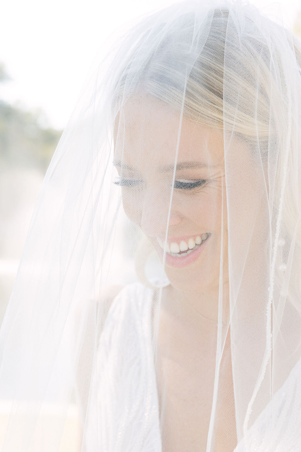 A joyful bride with a radiant smile is captured beneath her delicate veil during a Sea Pines wedding in Hilton Head. Soft, natural light enhances her elegance in this intimate bridal portrait. Wedding photographer Hilton Head Island. SC.