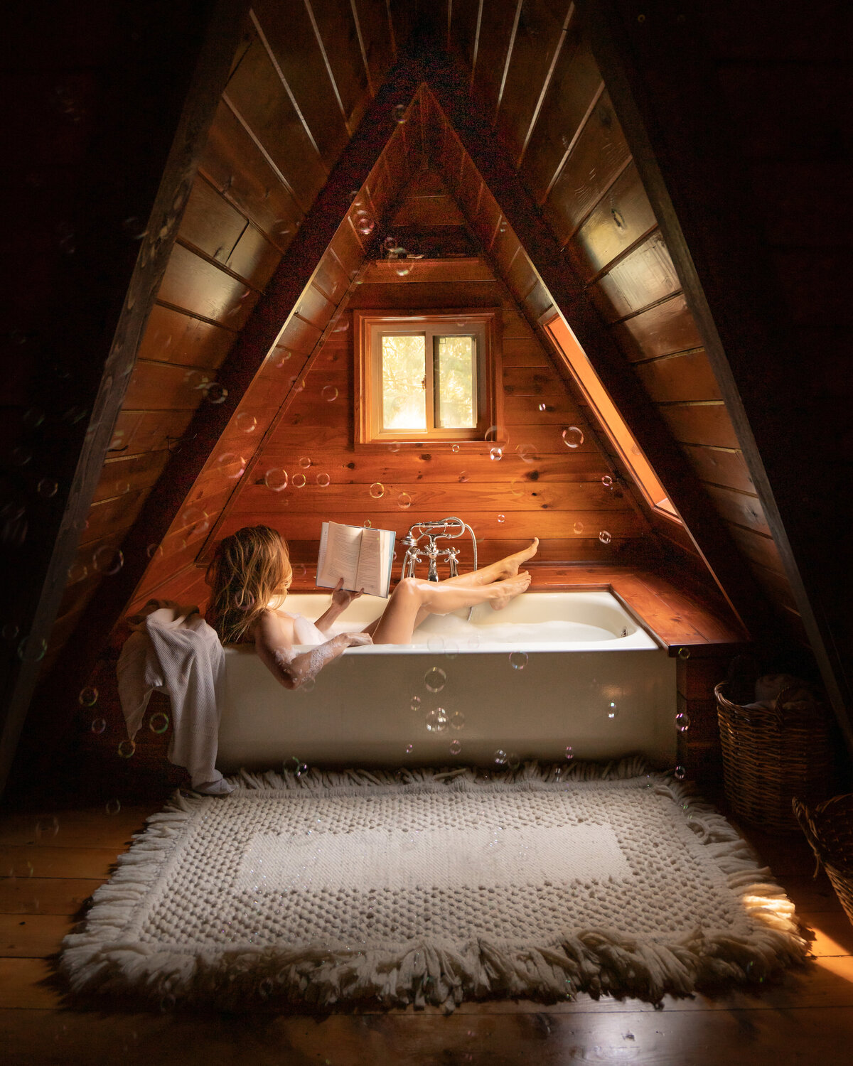 Woman lying in bathtub reading a book in an a-frame wooden cabin