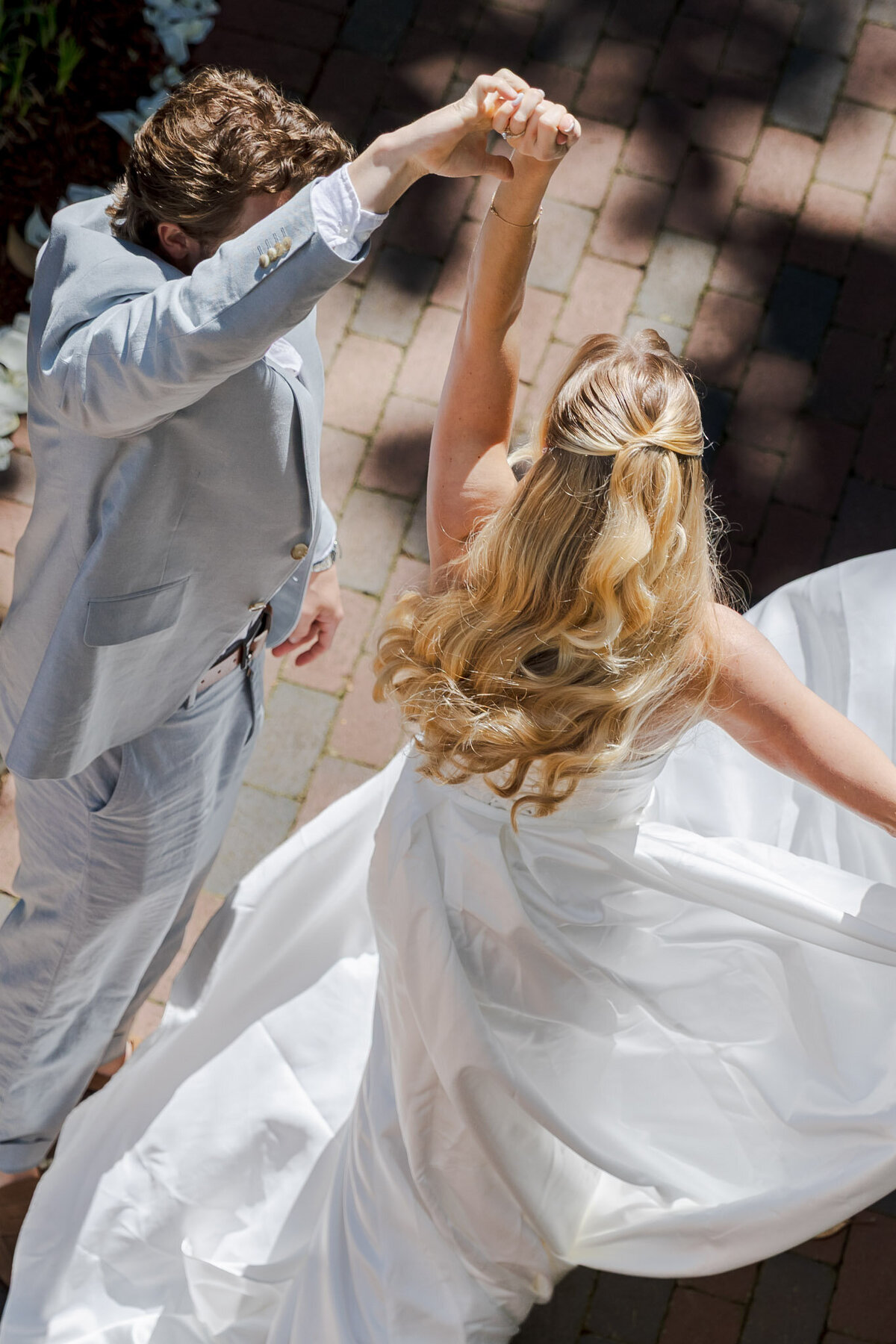 Bird's eye view of a bride and groom on their wedding day during their reception. The groom is twirling his bride. You can't see either of their faces.
