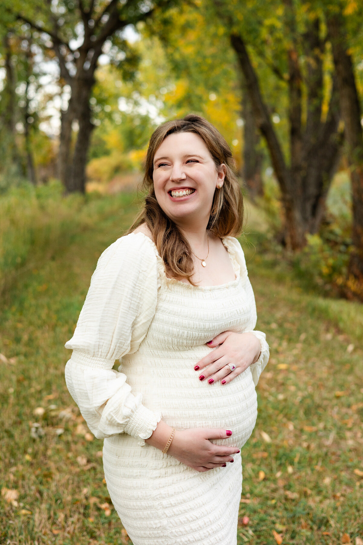 A pregnant woman holds her bump and smiles back over her shoulder.