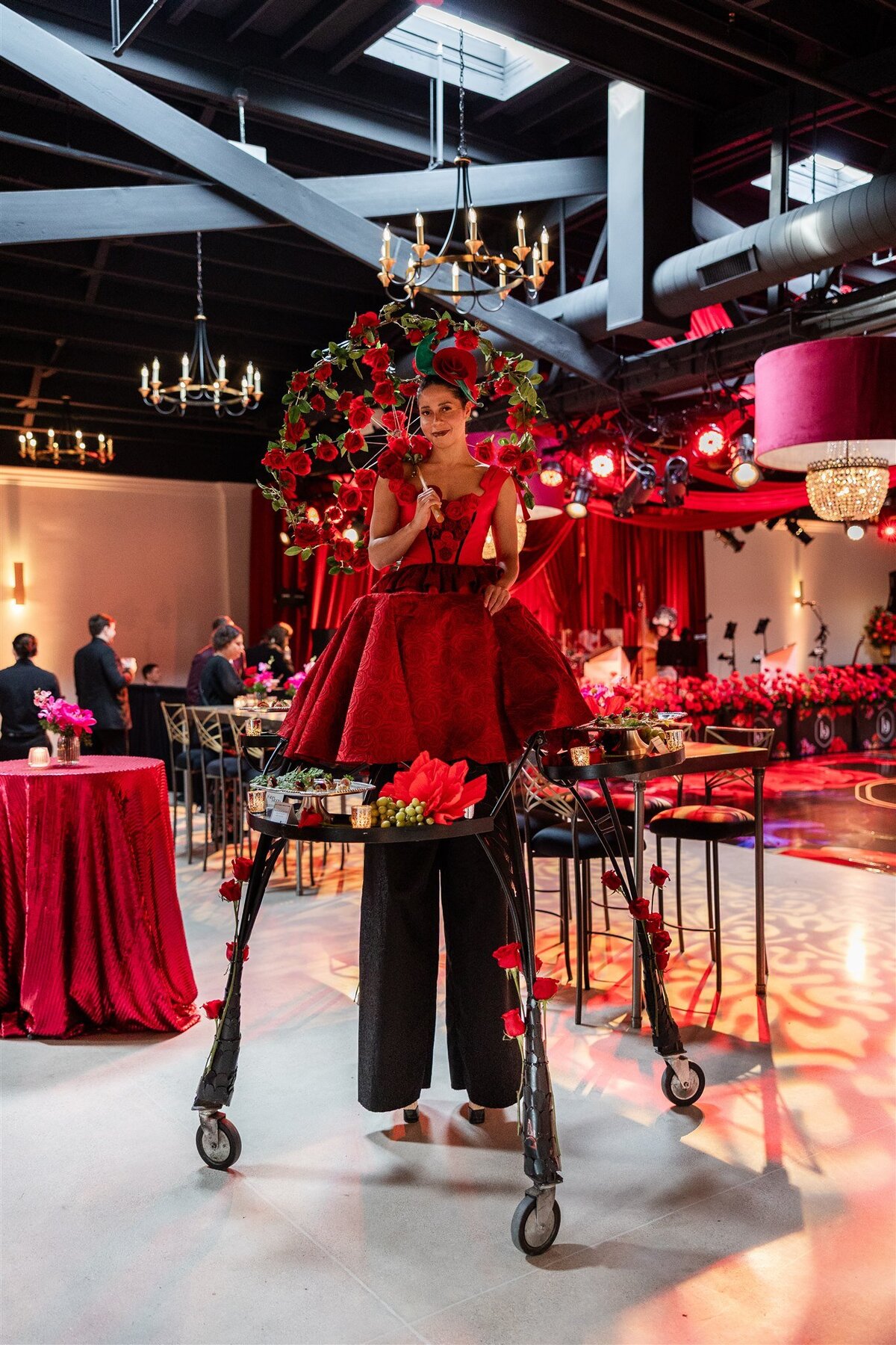 Woman on stilts dressed in an eye-catching outfit, playfully handing out food to guests, adding a whimsical and theatrical element to the event atmosphere