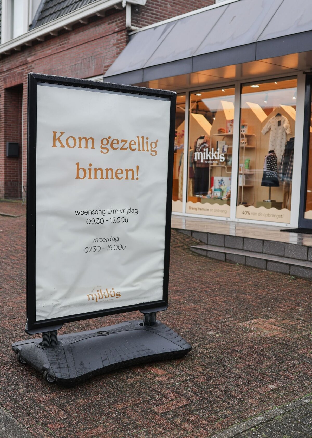 Een stoepbord voor een winkel met de tekst 'Kom gezellig binnen!' en de openingstijden.
