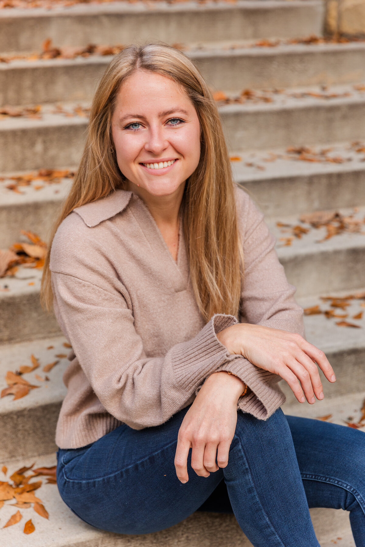 young woman wearing blue jeans ans a beige sweater sitting on outdoor steps during portraits