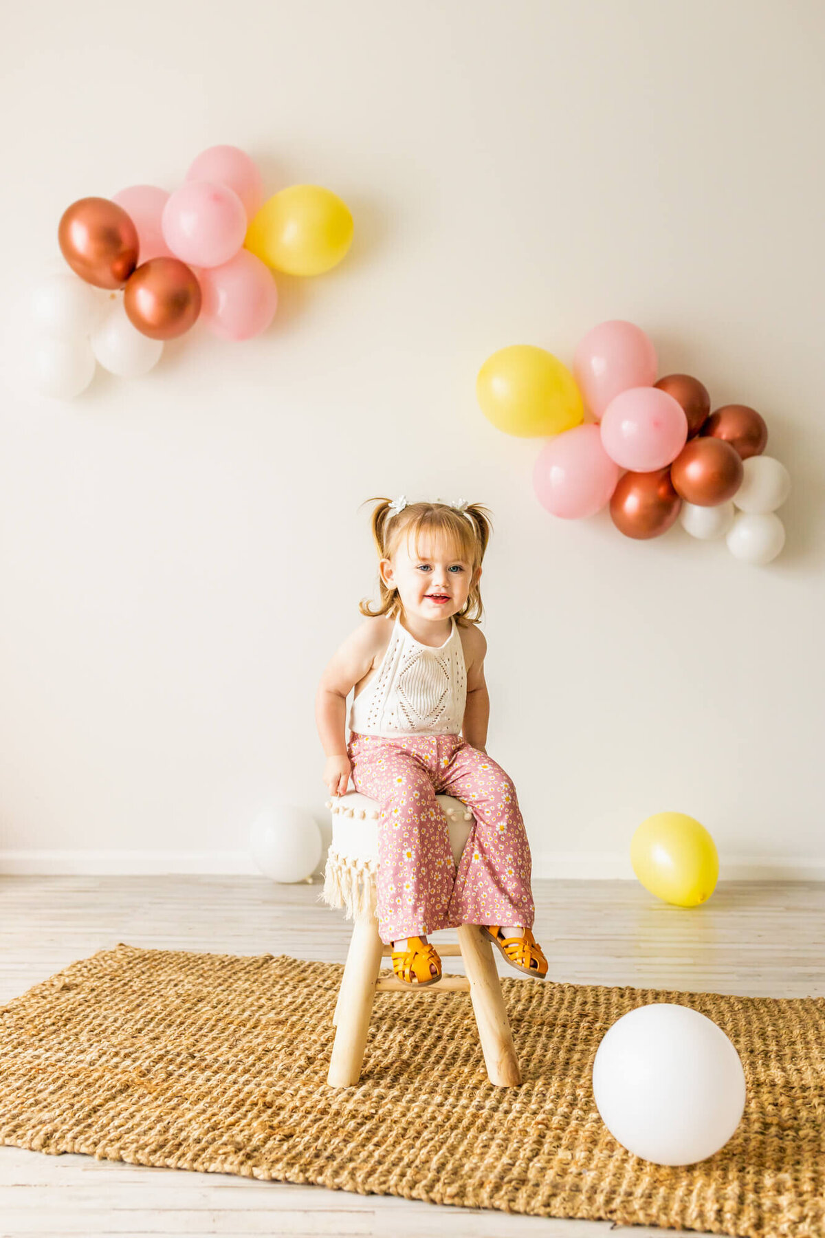 Toddler girl dresses in bell bottoms and a lace romper sitting on a boho chair
