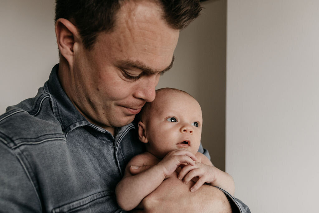 Vader knuffelt newborn baby tijdens de newbornshoot op de babykamer