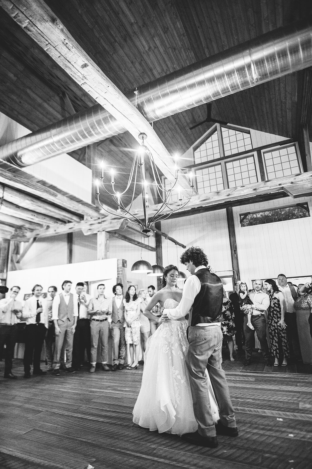 a black and white image of a bride and groom sharing their first dance together under the twinkling large chandelier at Willowbrook wedding venue