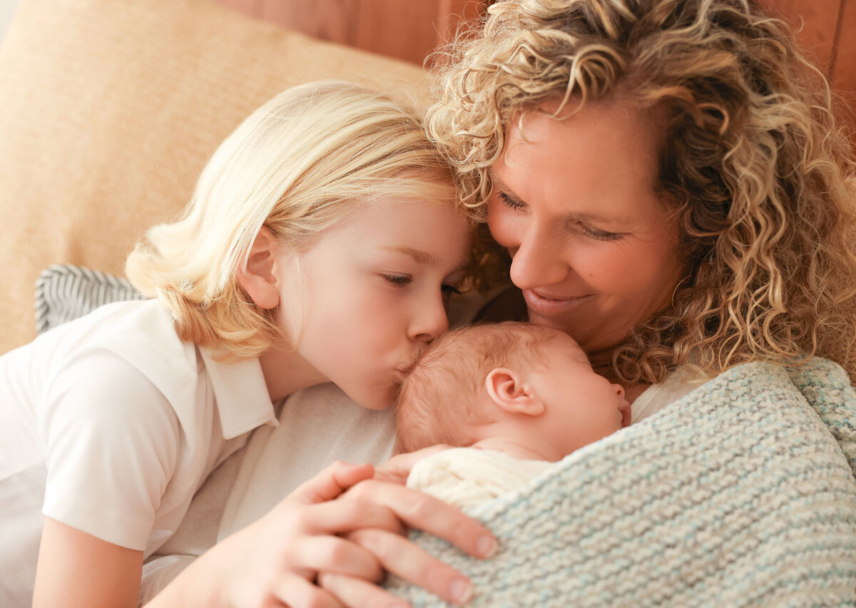 sibling love to new baby while laying on mom