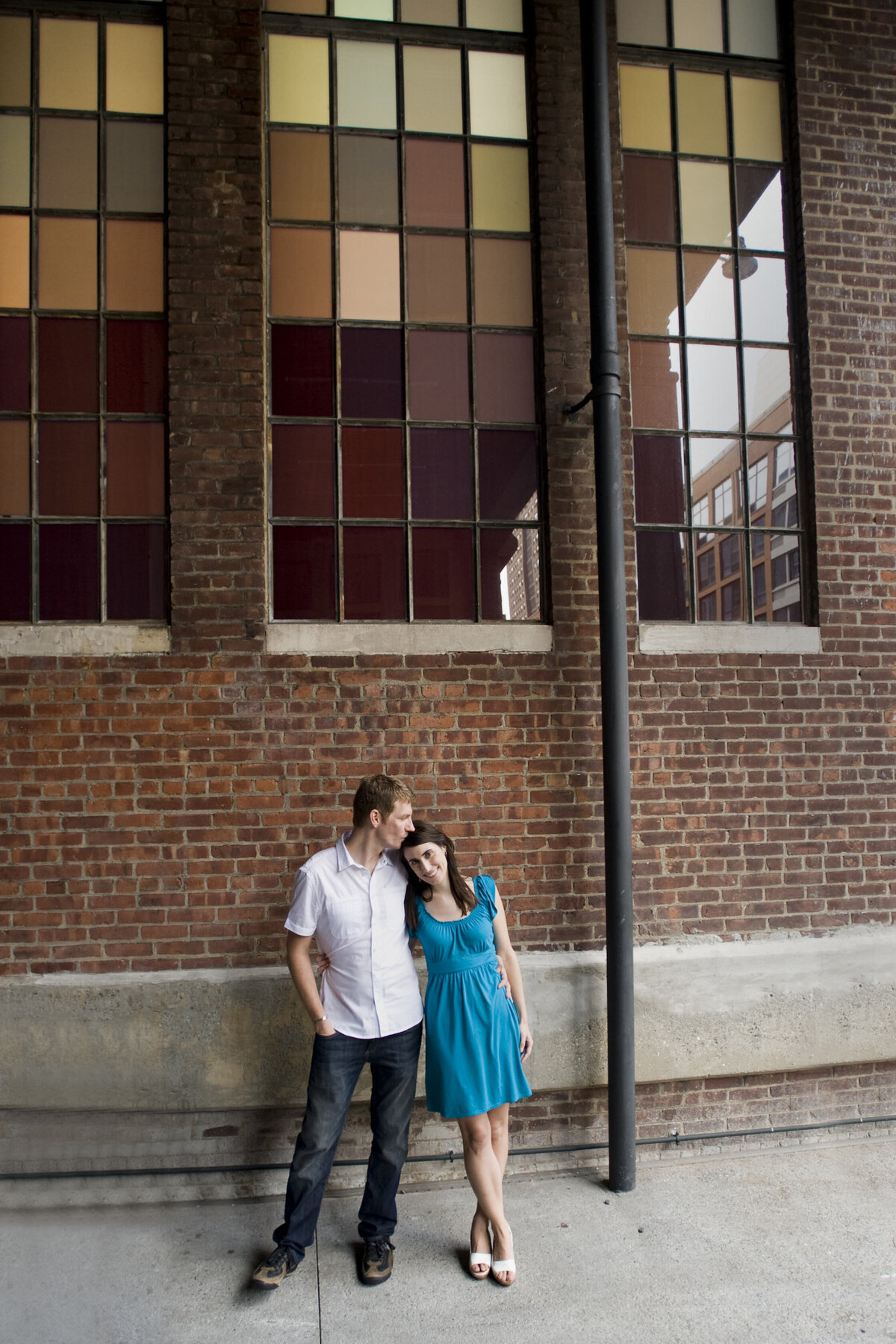 A couple standing side by side leaning against each other in front of a brick building 
