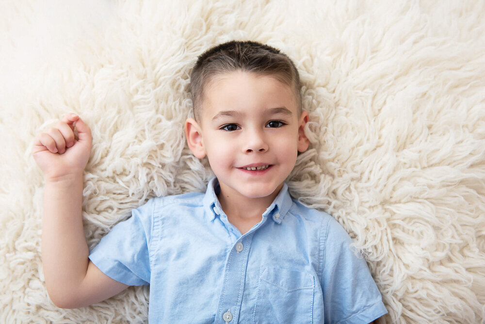 older boy laying on a cream rug.
