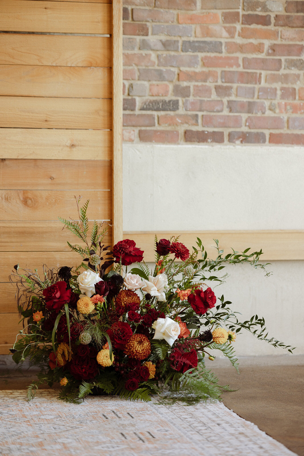 Flower arrangement with burgundy, red, orange, and white flowers.