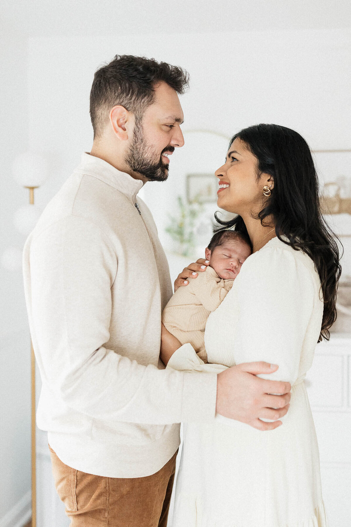 Joyful parents smiling at each other while holding sleeping newborn in Shaker Heights home.