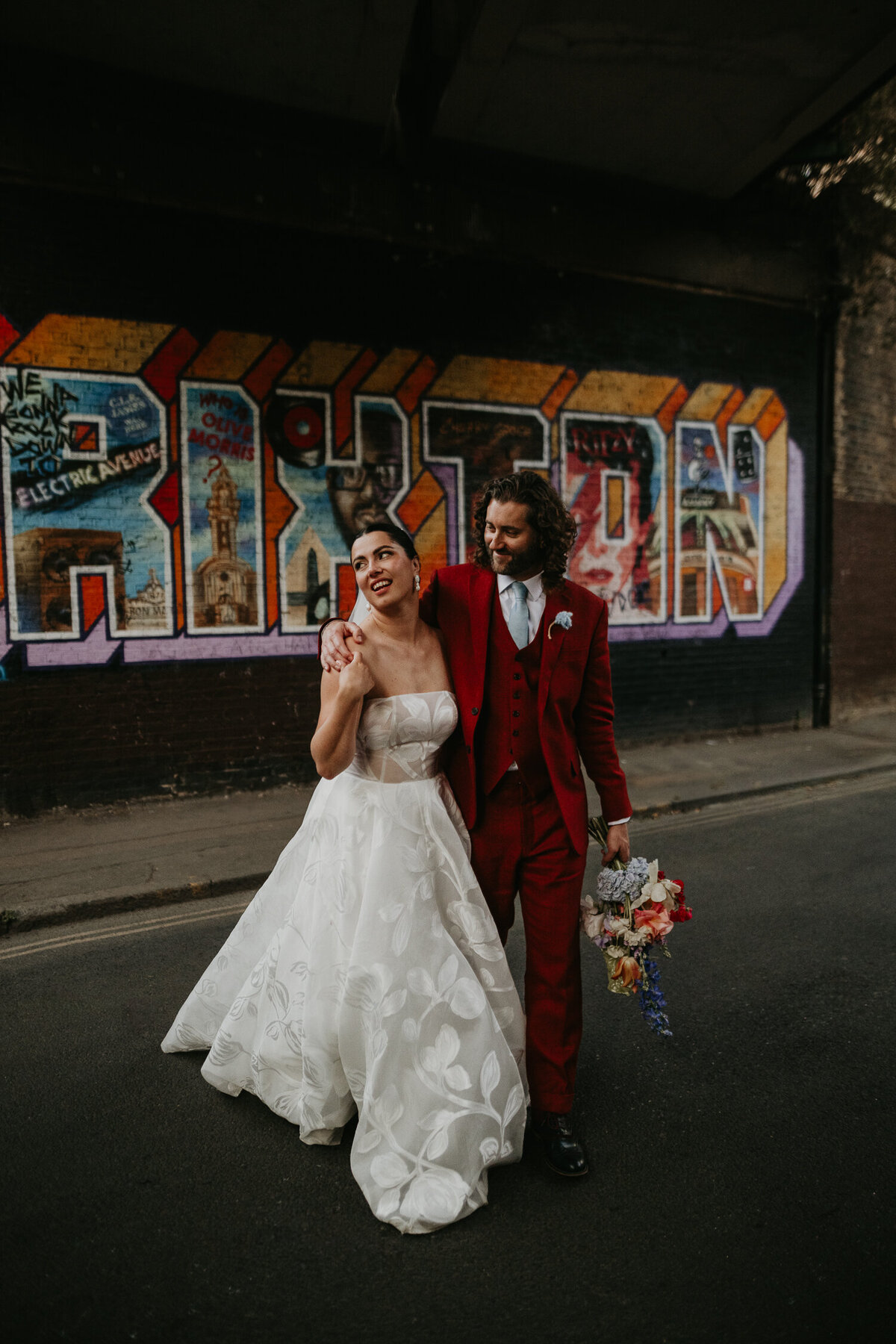 A bride and groom walk in front of the Brixton mural near 100 Barrington in London. 