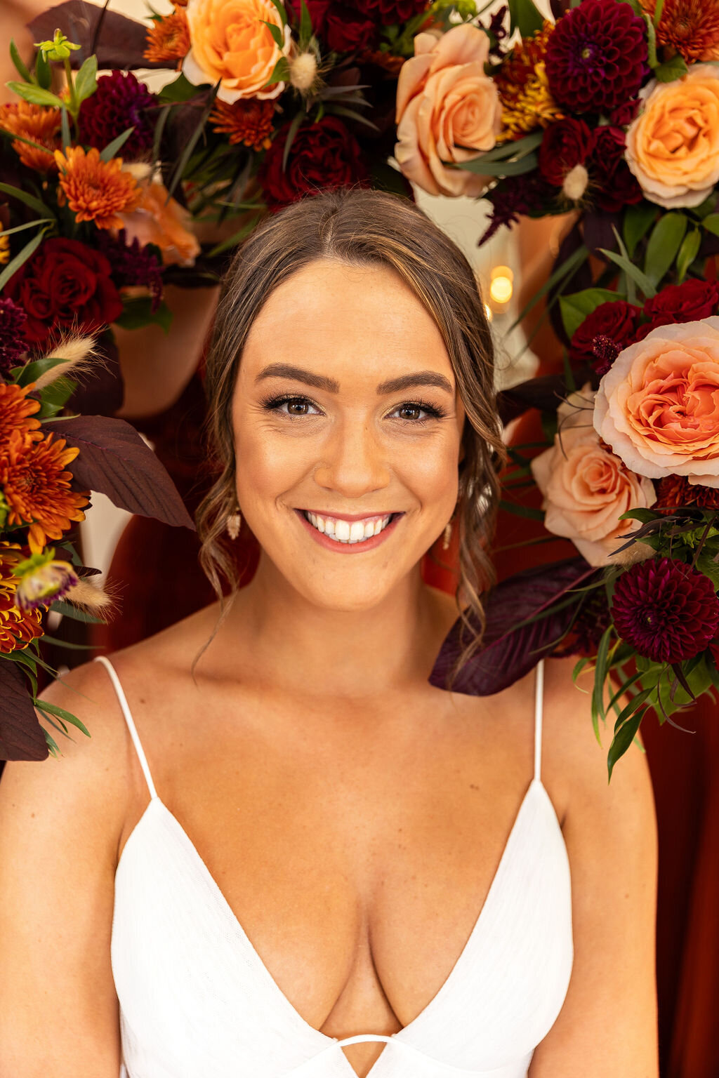 Bride surrounded by her bridesmaids bouquets on her wedding day with burgundy, peach, and orange flowers.