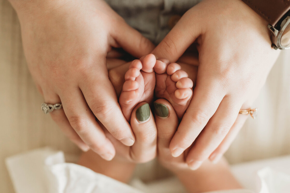 Two mothers make a heart with their hands around their newborn baby's feet.