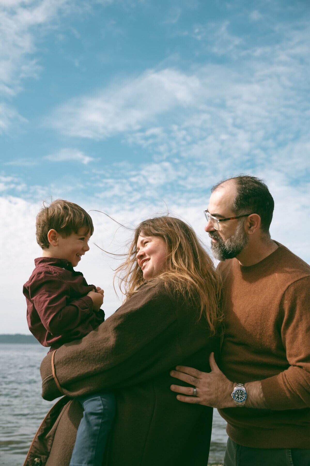 a male and female holding toddler at beach wearing neutral clothing colors