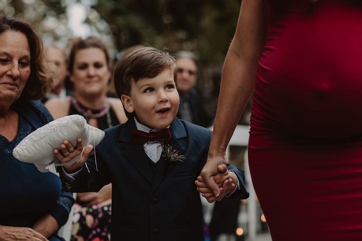 A small child walking down the aisle with an adult as they are the ring bearer at a wedding 