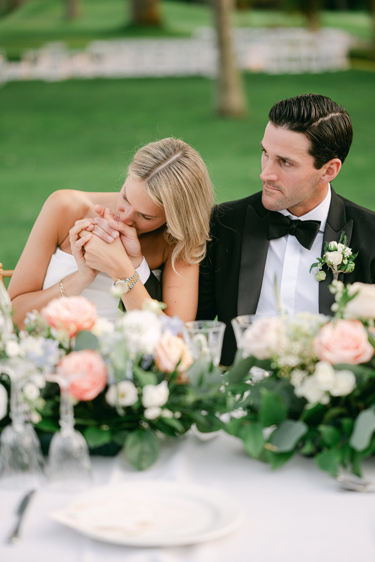 Blonde bride kisses grooms hand during an emotional speech at their wedding reception