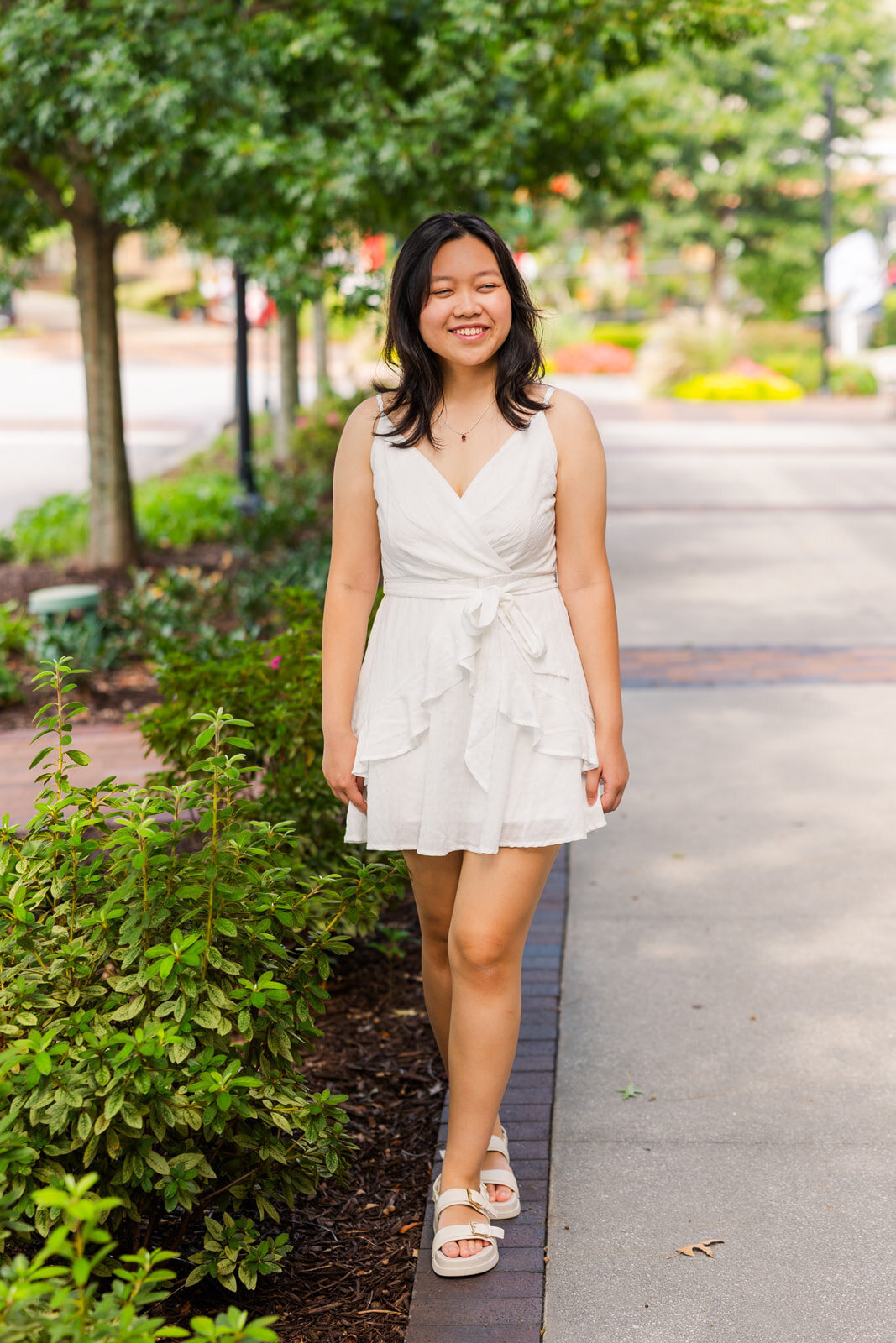 Senior girl walking towards the camera and looking sideway in a street sidewalk during portrait photo session
