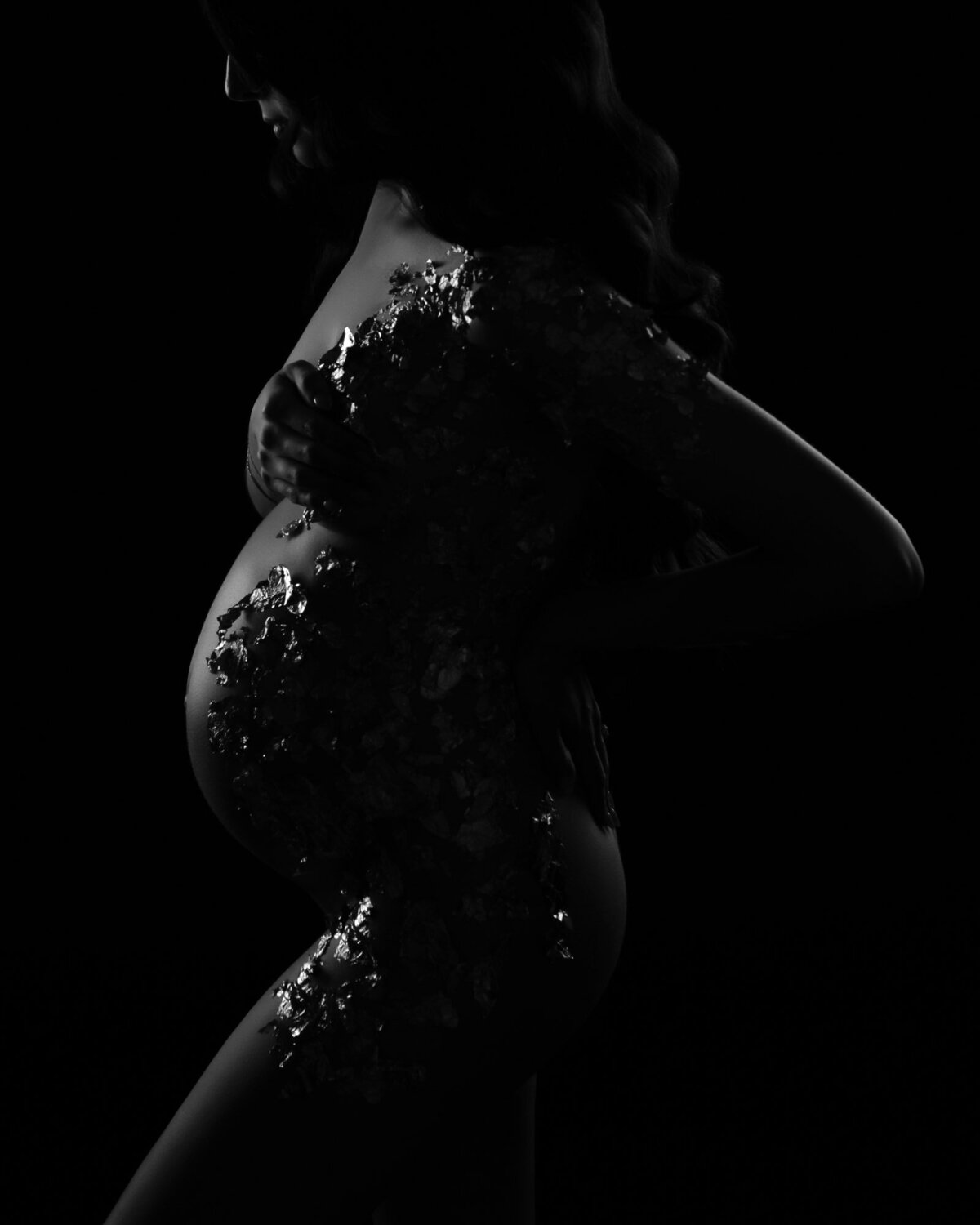 Artistic black and white maternity silhouette with dramatic studio lighting showcasing pregnant profile
