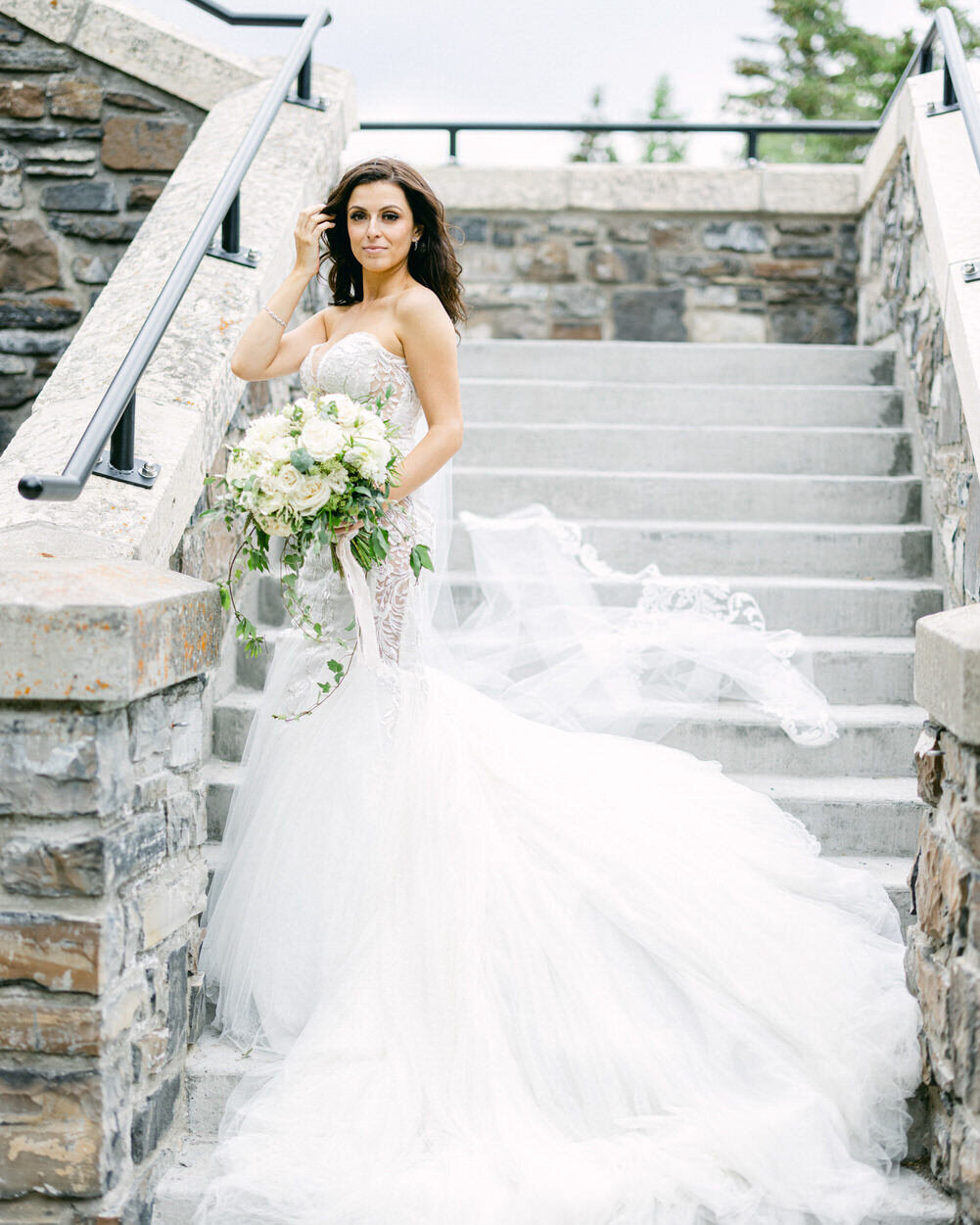 This stunning portrait captures the bride standing gracefully on the stairs outside the Banff Springs Hotel during her luxury wedding. The grand architecture and picturesque surroundings enhance the timeless beauty and sophistication of the moment.
