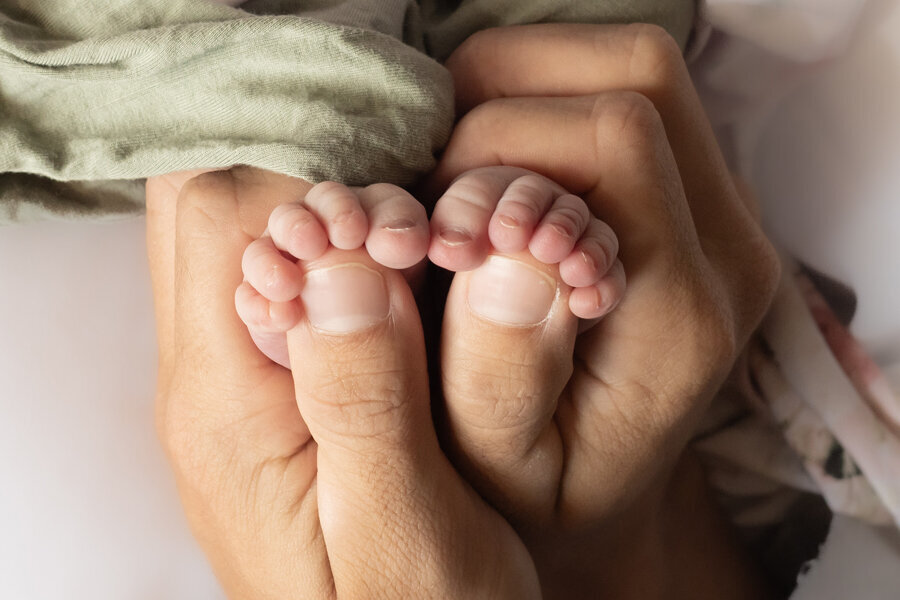 Hands holding baby feet with toes wrapped over thumbs.