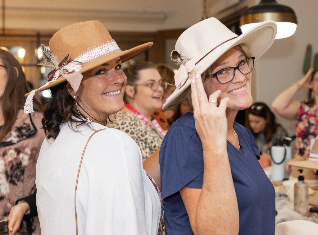 two women wearing the hats they just decorated