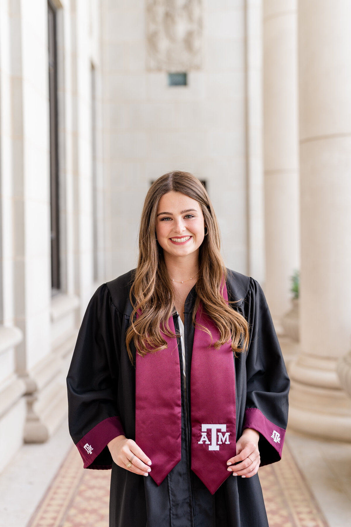 Texas A&M senior girl wearing gown and Aggie stole and smiling in the columns of the Administration Building