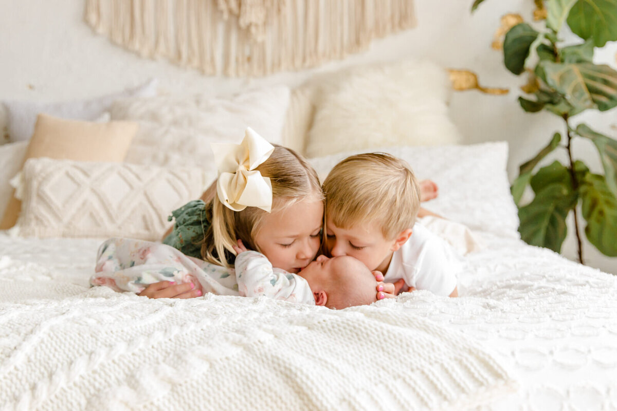 Brother and sister kiss their newborn baby sister on the head during her newborn session in Buford