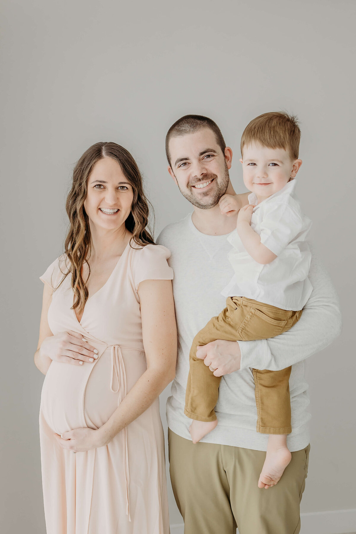 Family portrait of young couple expecting baby while dad holds son
