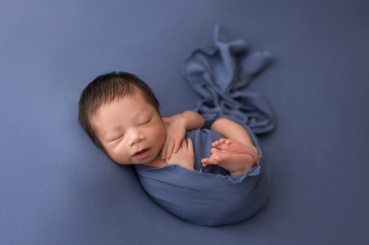 Newborn baby wrapped in a blue blanket, peacefully sleeping on a blue background.