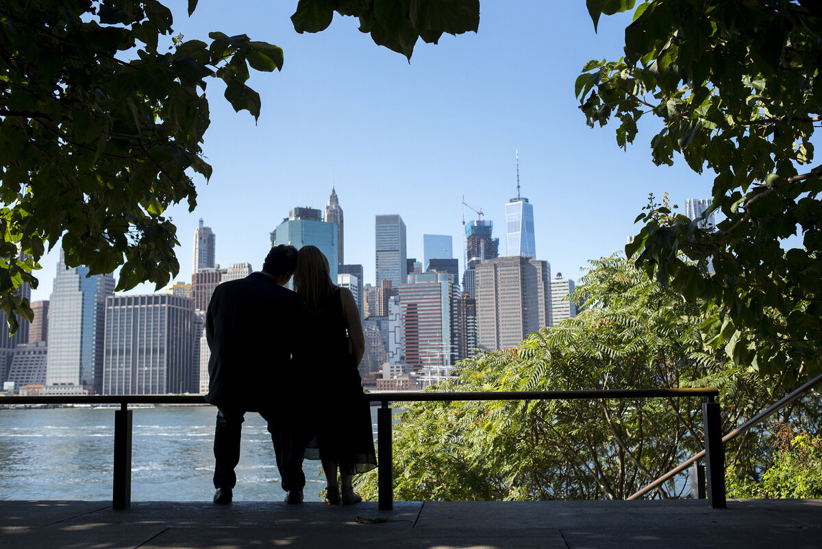 A couple sitting together and leaning against each other looking out over a city skyline 