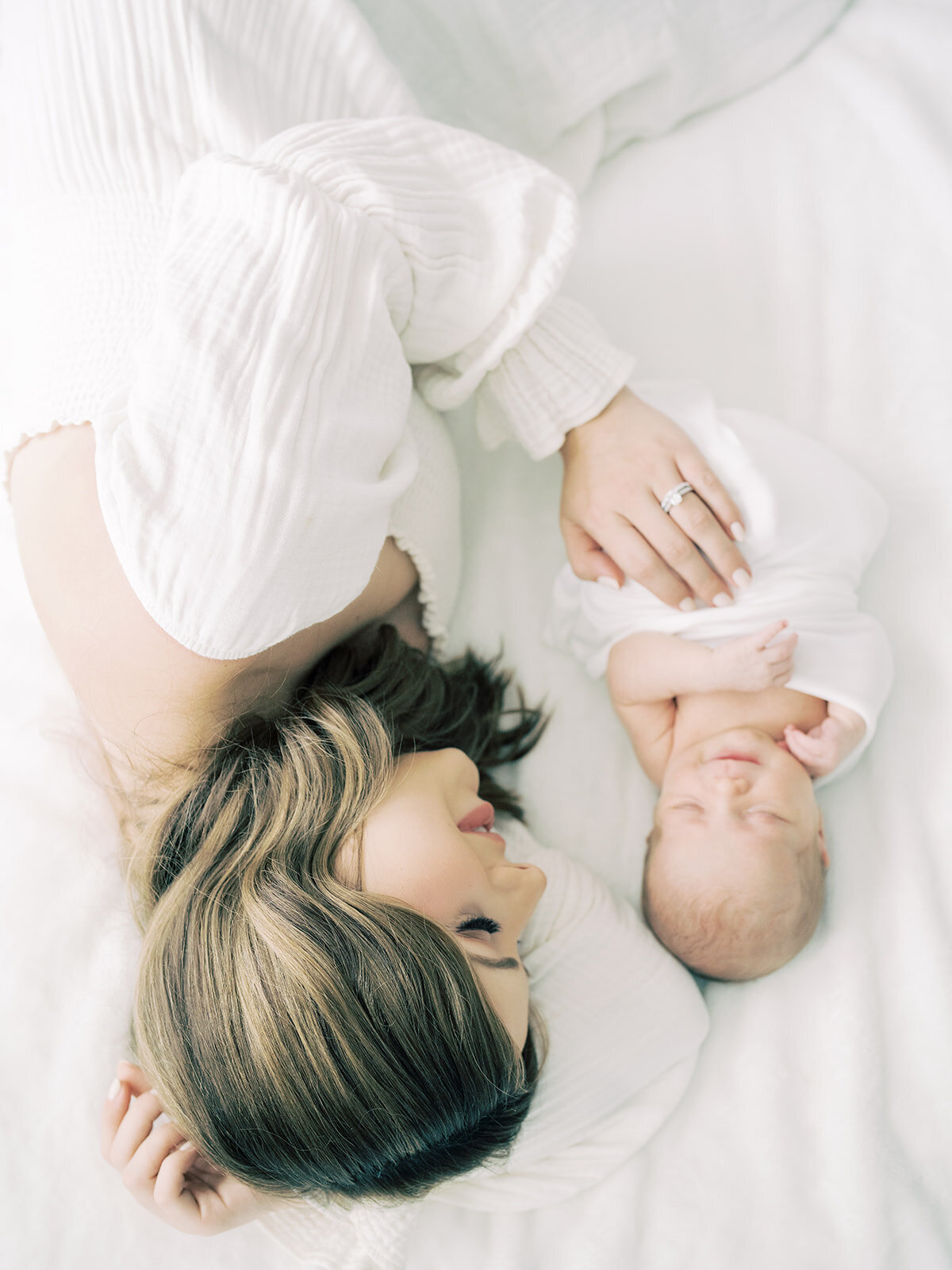 Mother with brown hair lays down on bed with newborn baby girl during her Maryland newborn session.