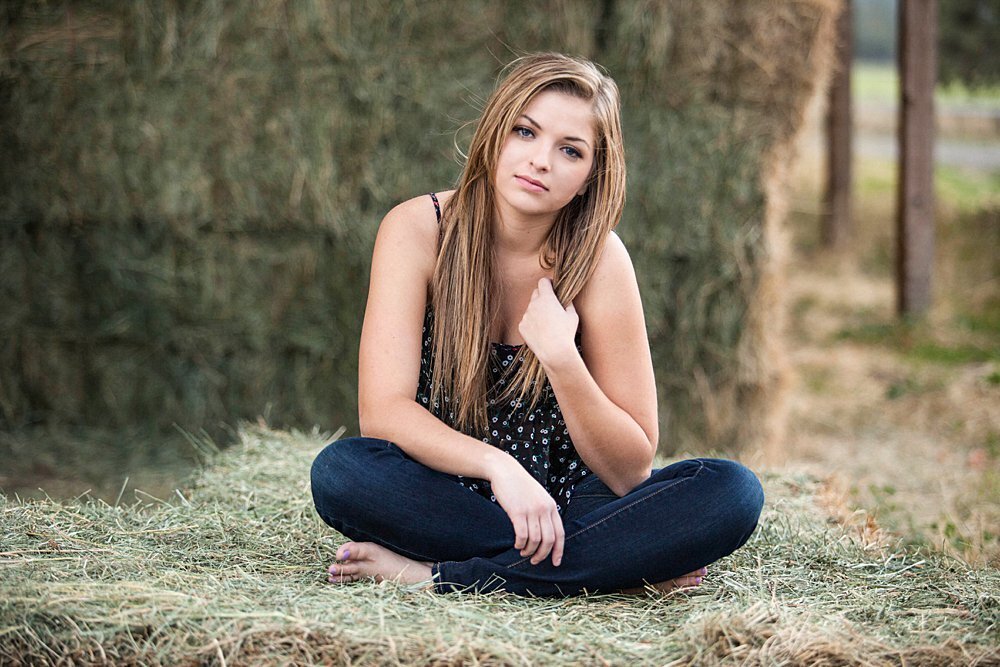 Country senior girl sitting on hay bale