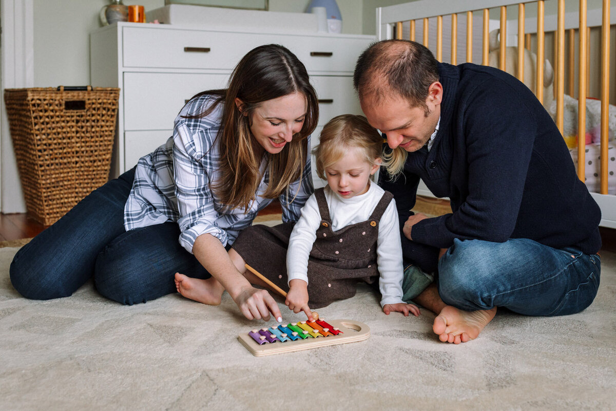mom and dad playing with a xylophone with their 4-year-old daughter in her bedroom on the floor