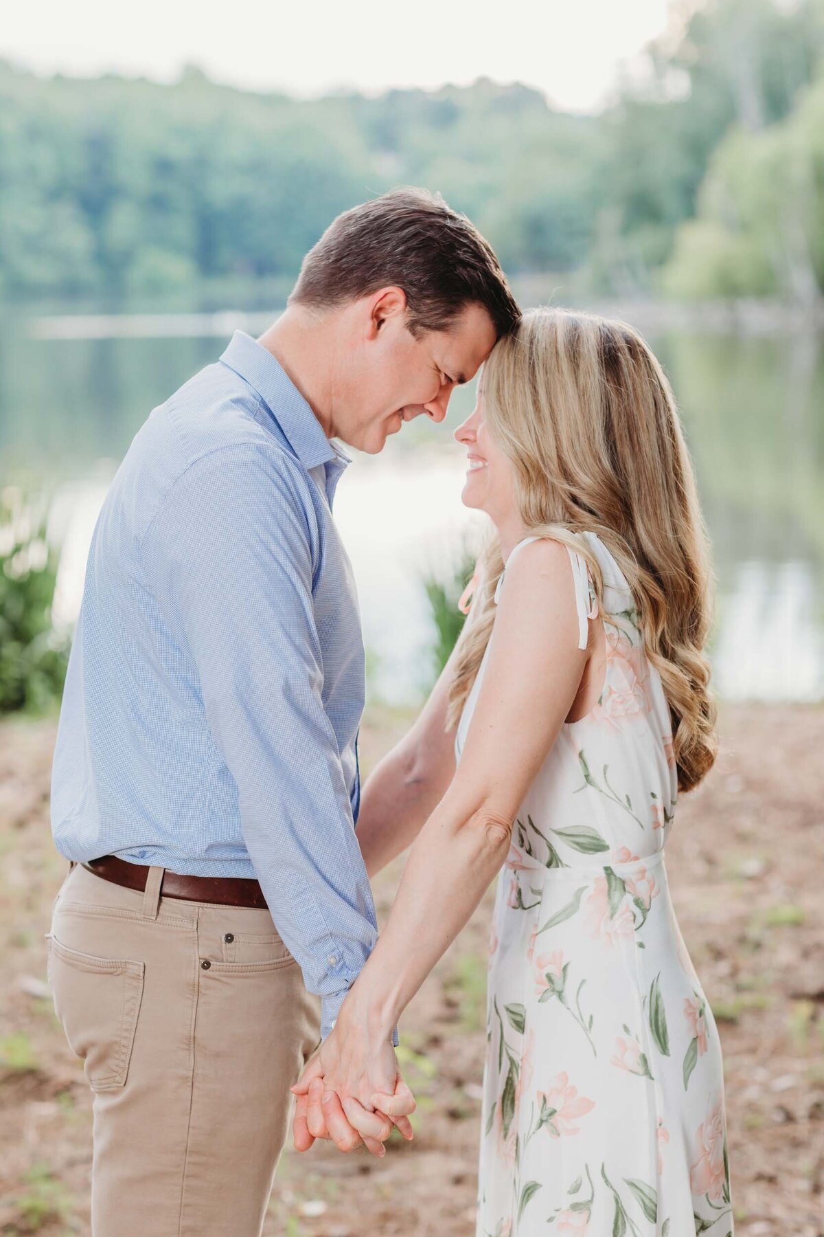 This couple is facing each other and touching foreheads while they grin at each other in front of Lake Peachtree in Peachtree City.